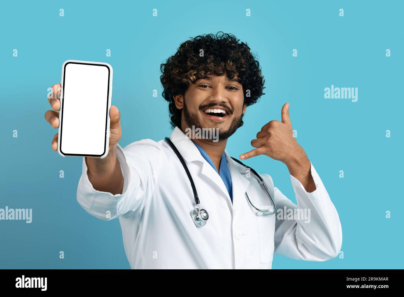 Positive handsome young indian doc showing phone with mockup Stock Photo