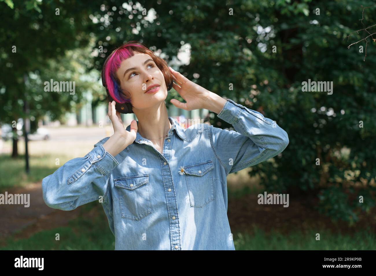 Woman with pink hair with headphones listens to music in the park Stock Photo