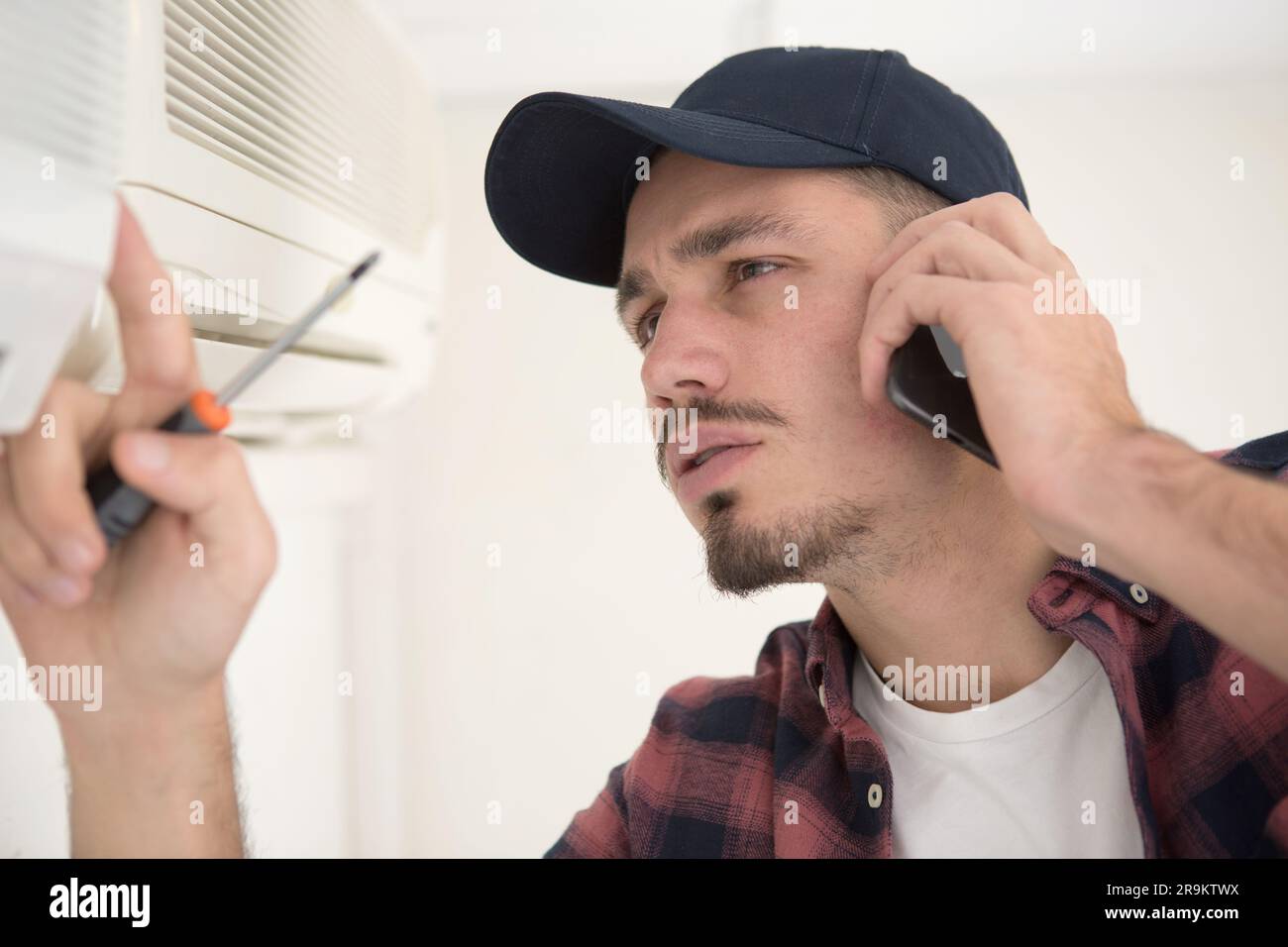 young handyman repairing air conditioning system calling for help Stock Photo