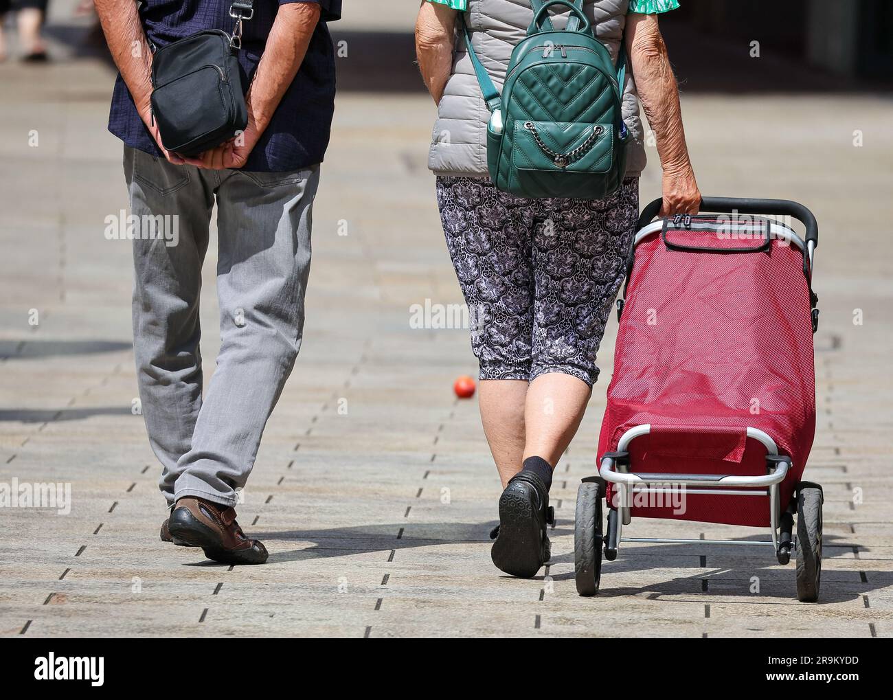 Leipzig, Germany. 27th June, 2023. A senior couple in breezy casual wear walks through downtown Leipzig with a shopping trolley. The approximately 21 million pensioners in the country will receive more money starting in July. With the annual pension adjustment, retirement benefits will rise by 4.39 percent in the west and 5.86 percent in the east. In addition, almost 30 years after reunification, the so-called pension value in the east will be brought into line with that in the west - one year earlier than planned. Credit: Jan Woitas/dpa/Alamy Live News Stock Photo