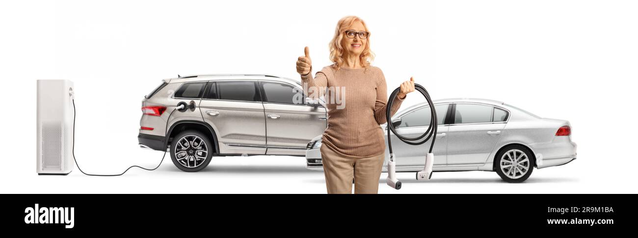 Woman holding cables for EV charging in front of electric cars and gesturing thumbs up isolated on white background Stock Photo