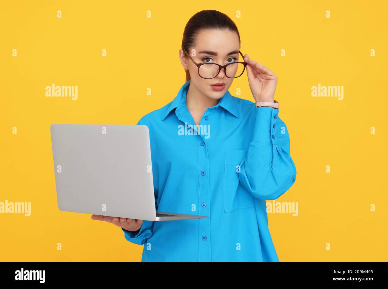 Young female intern with laptop on yellow background Stock Photo