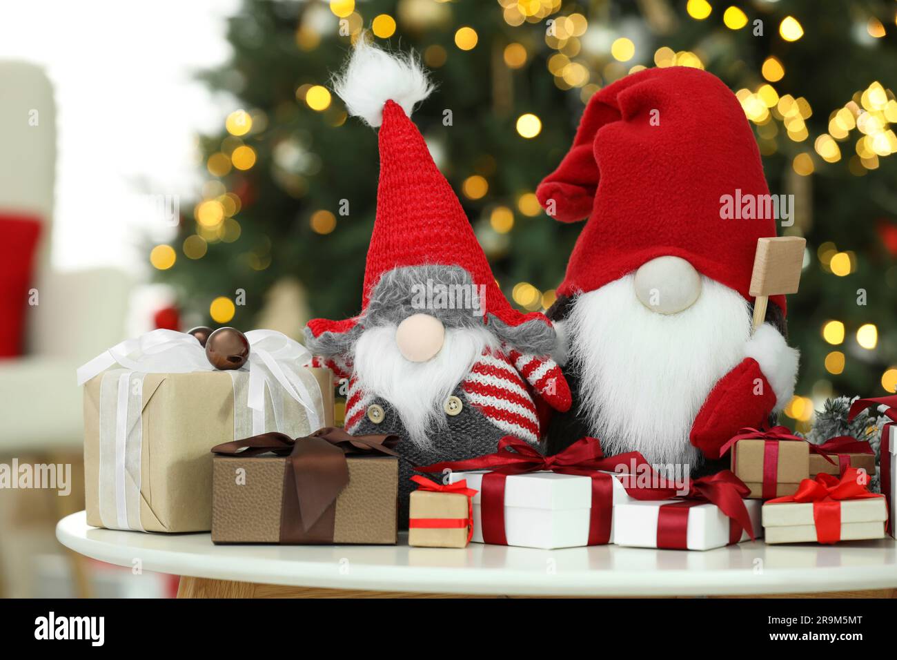 Funny Christmas gnomes and gift boxes on coffee table in room with