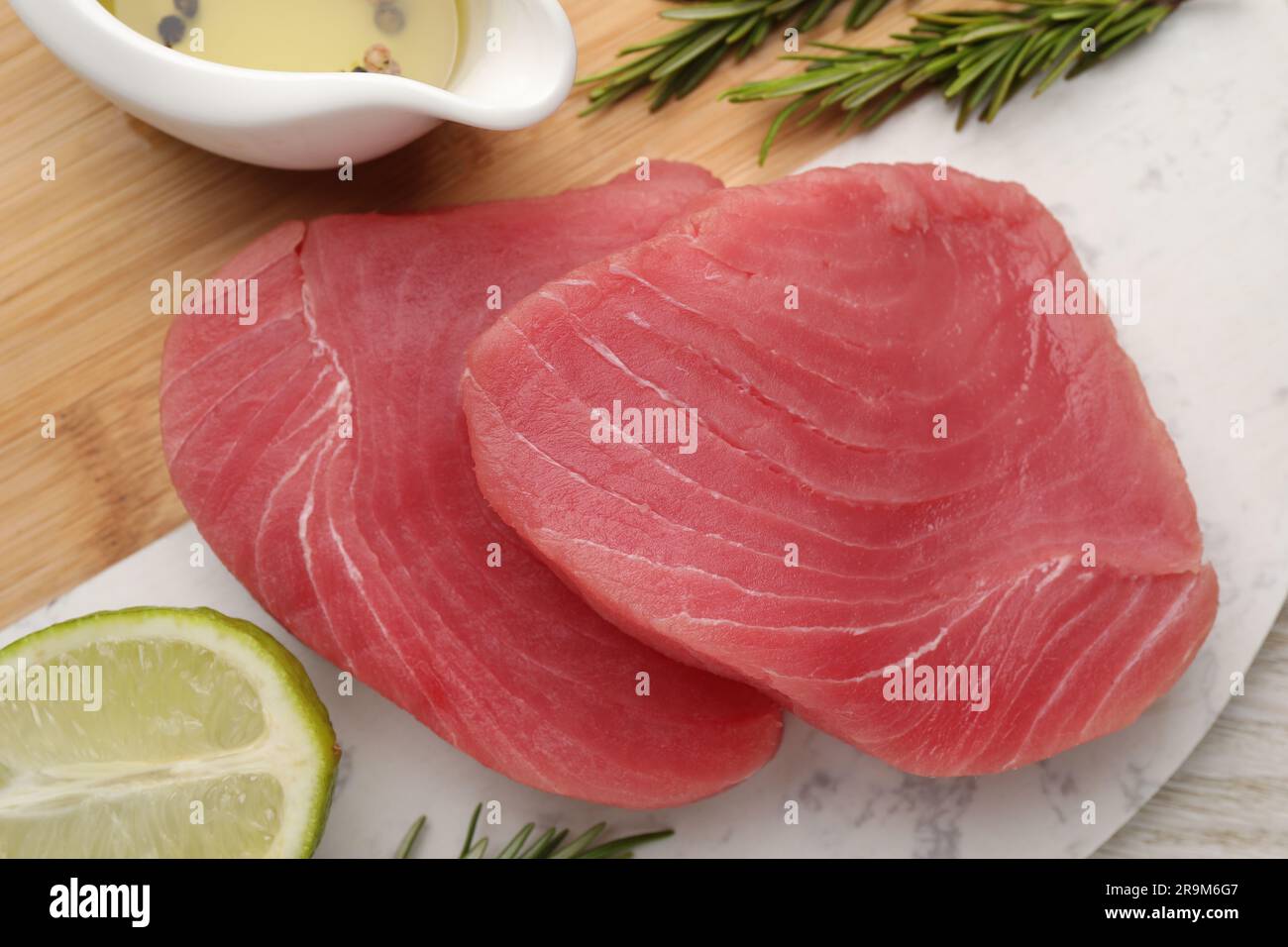 Raw tuna fillets with rosemary, lime and oil on board, top view Stock