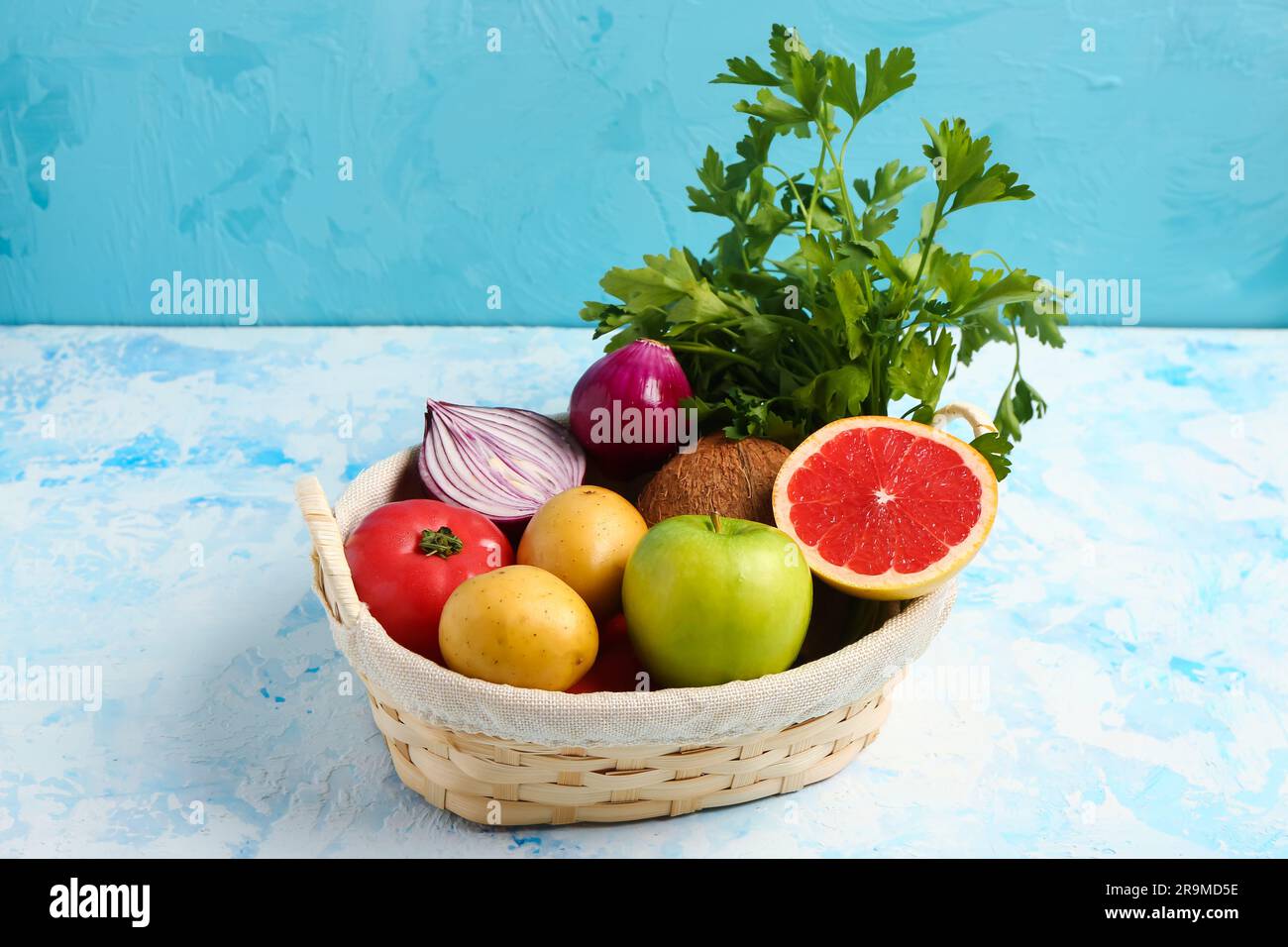 Wicker basket with different fresh fruits and vegetables on blue ...