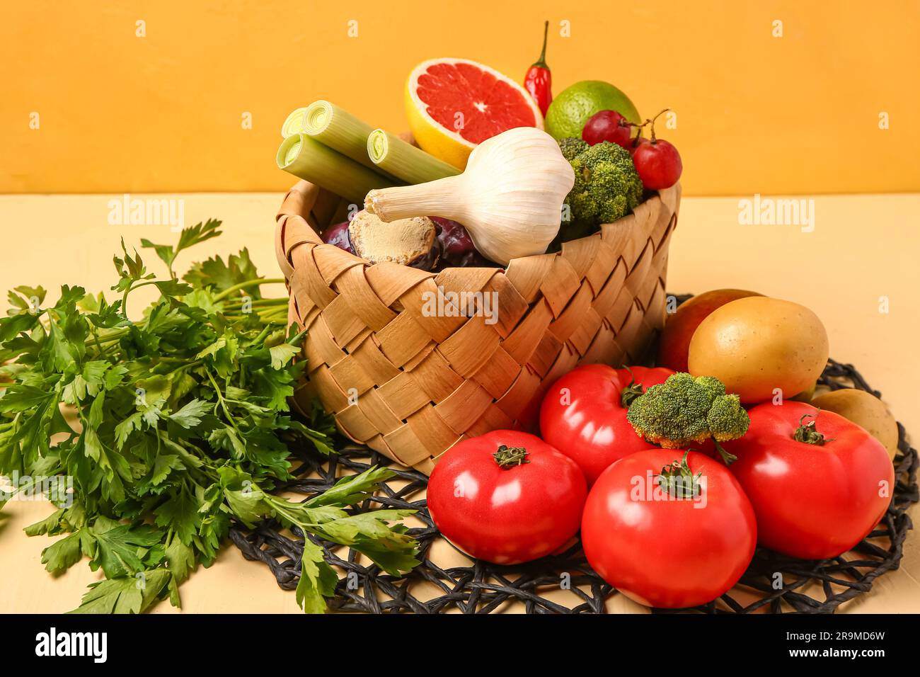 Wicker basket with different fresh fruits and vegetables on yellow ...