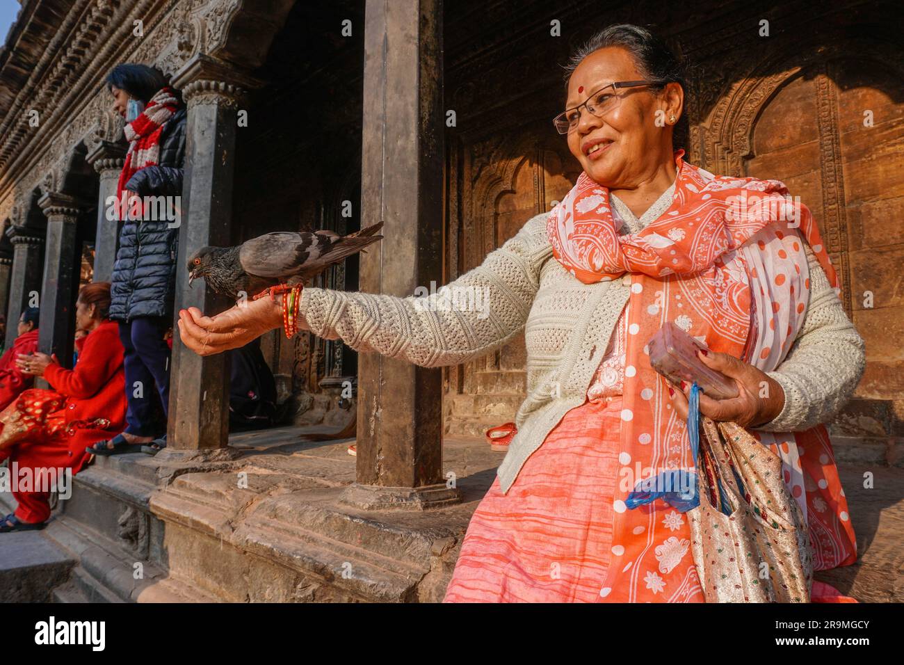 Lalita Chaudhary feeds a pigeon rice from her hand at Patan Durbar Square in Lalitpur, Bagmati province, Nepal on March 24, 2023. (Yam Kumari Kandel/Global Press Journal) Stock Photo