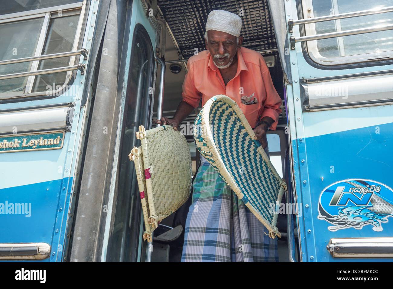 Mohitheen Lamalipu carries winnowing fans off a bus in Mannar, Sri Lanka on March 23, 2023. Every morning, Lamalipu comes to a city bus station, where he boards every bus ready to depart to sell baskets to passengers. (Vetrichelvi Chandrakala/Global Press Journal) Stock Photo
