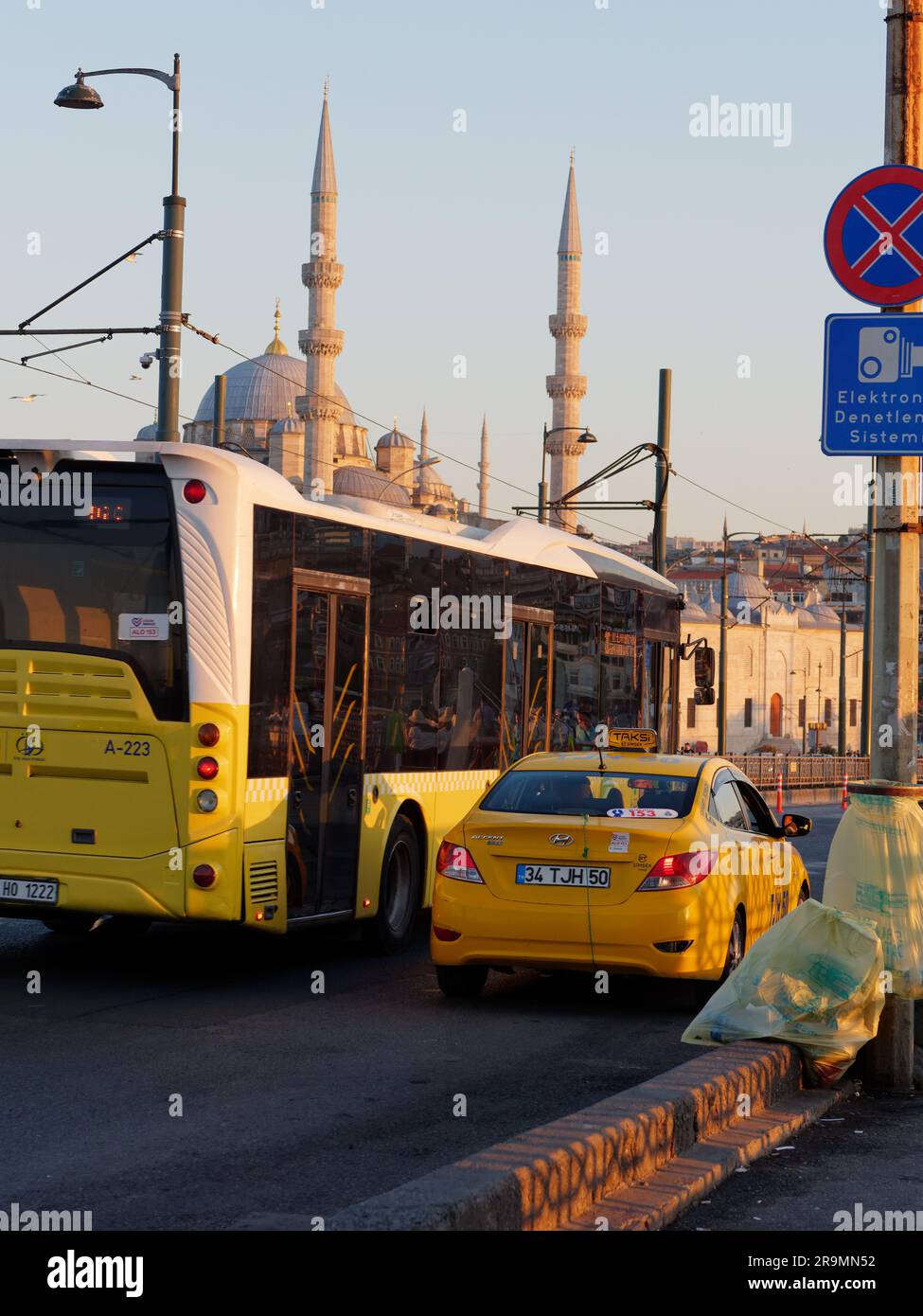 Traffic in Istanbul on a summers evening with a yellow Taxi and a yellow and white bus on a strreet with a Mosque behind. Turkey Stock Photo