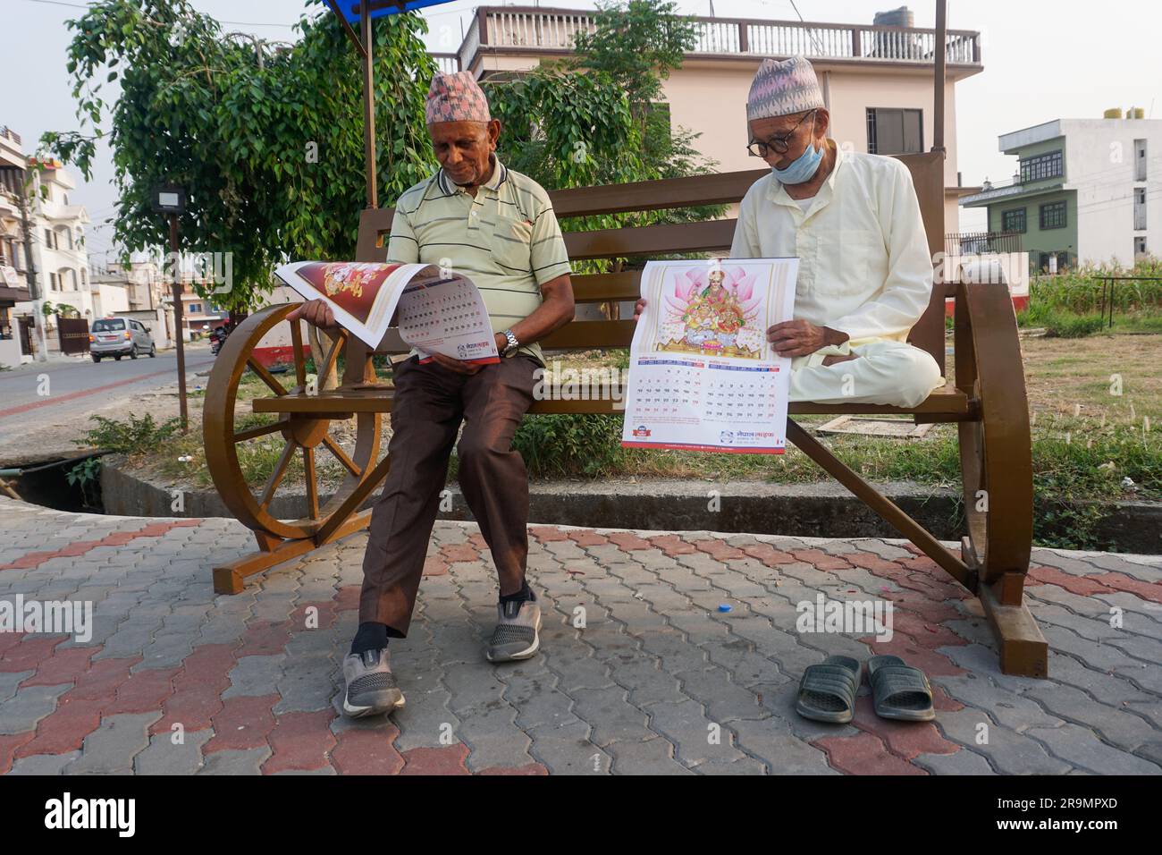 Govinda Prasad Kadariya, left, and Yogyanath Pokharel peruse an insurance company’s promotional calendars at a park in Birtamod, Jhapa district, Nepal on May 15, 2023. They became good friends two years ago and come to the park together every evening. (Maya Neupane/Global Press Journal) Stock Photo