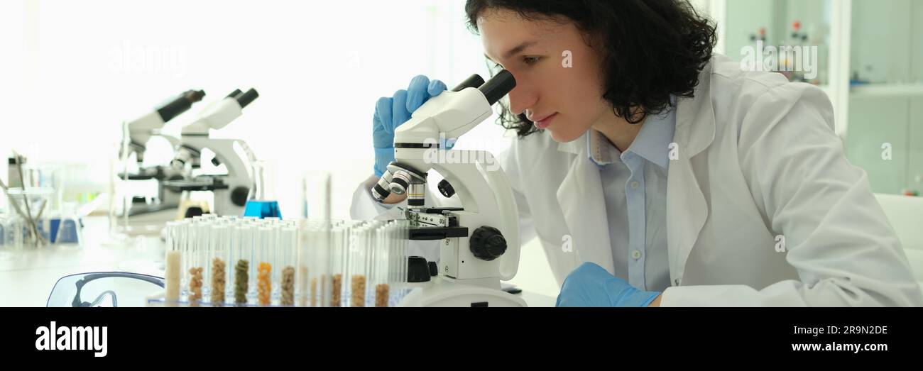 Scientist chemist looking through microscope in front of test tubes ...