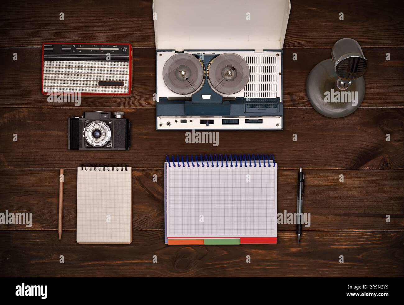 Old retro reel tape recorder, vintage radio, retro camera on wooden table. Blank notepad and pen. Stock Photo