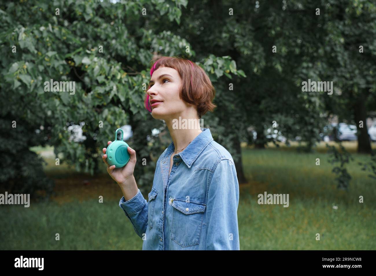 Woman with pink hair listens to music through the portable musical speaker in the park Stock Photo