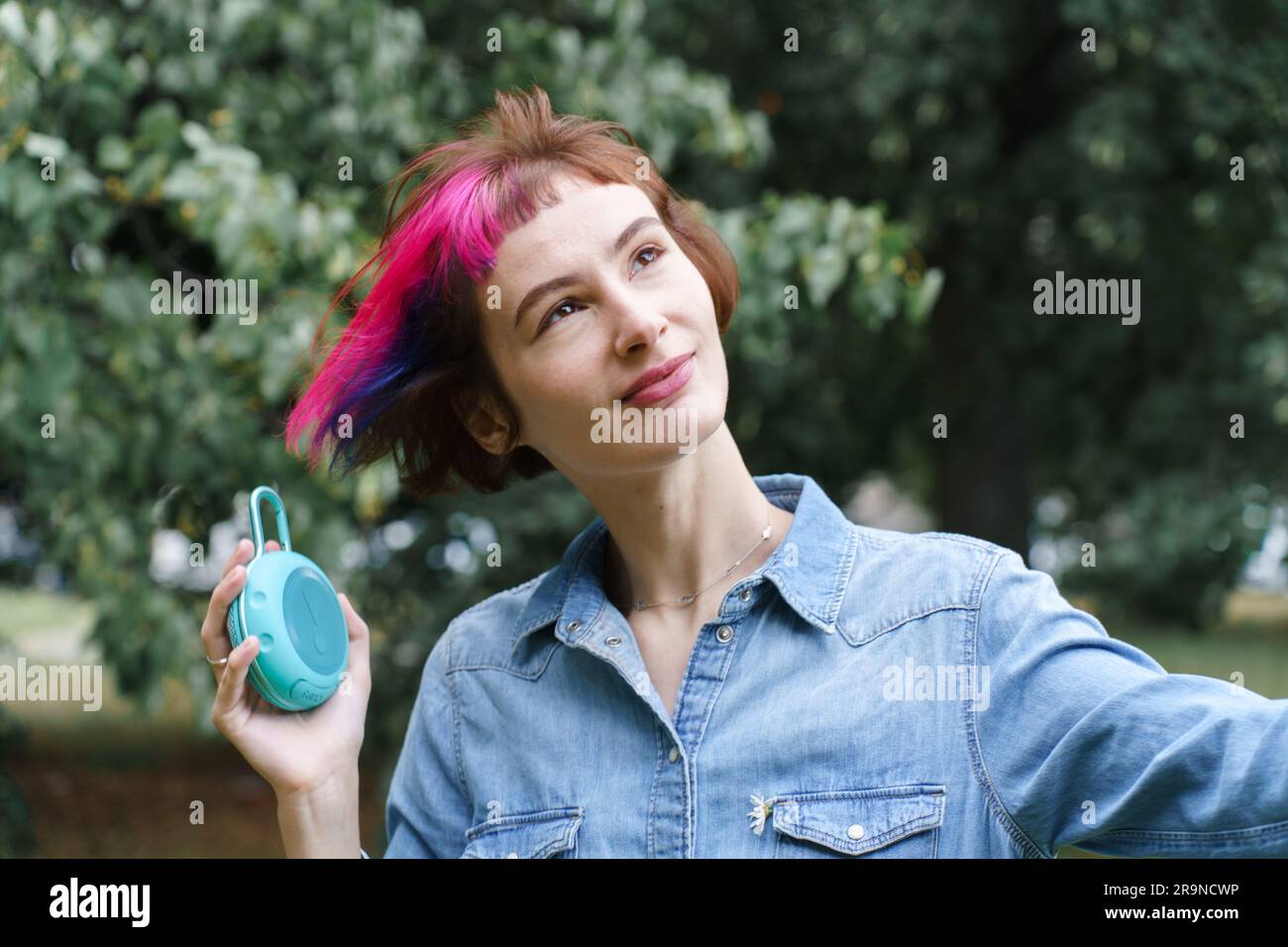 Woman with pink hair listens to music through the portable musical speaker in the park Stock Photo