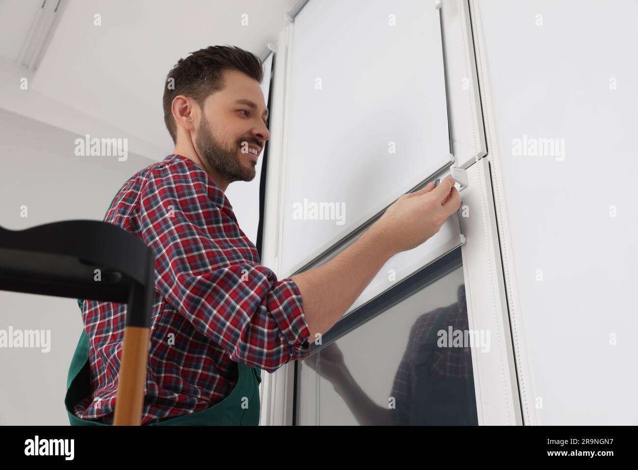 Worker in uniform installing roller window blind indoors Stock Photo