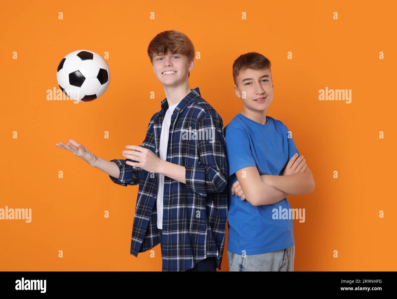 Happy teenage boys with soccer ball on orange background Stock Photo
