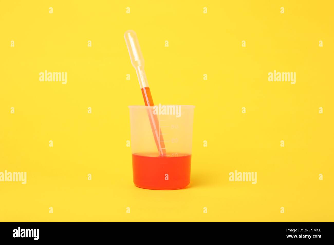 Beaker with liquid and stirring rod on yellow background. Chemical experiment toy for kids Stock