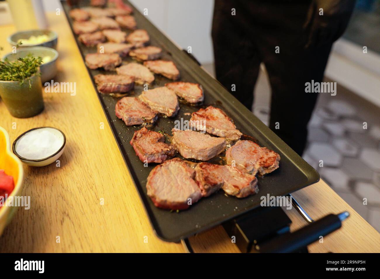 Shallow depth of field (selective focus) details with beef steak being cooked by a chef on a stove with butter, salt and rosemary. Stock Photo