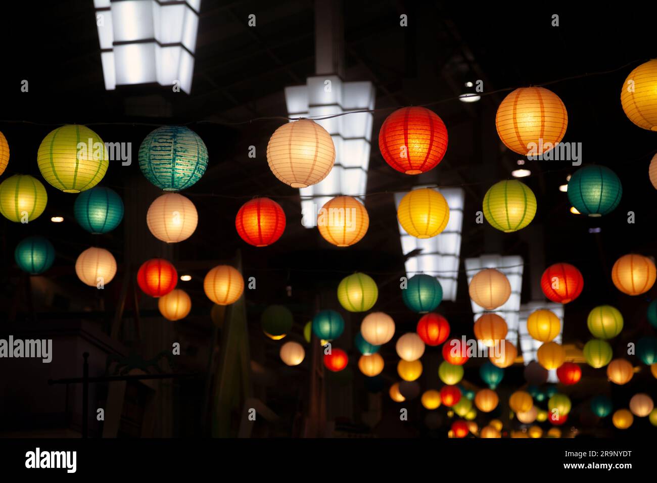 Many round Chinese paper lanterns hanging in the dark. A lot of festive colorful decorations prepared for a holiday celebration in an oriental style - Stock Image