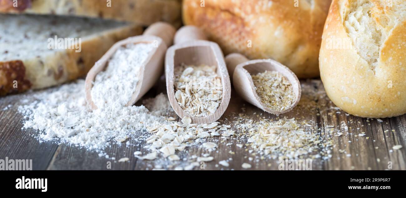 Wooden scoops of wheat flour, oats and oat bran with bread and buns in