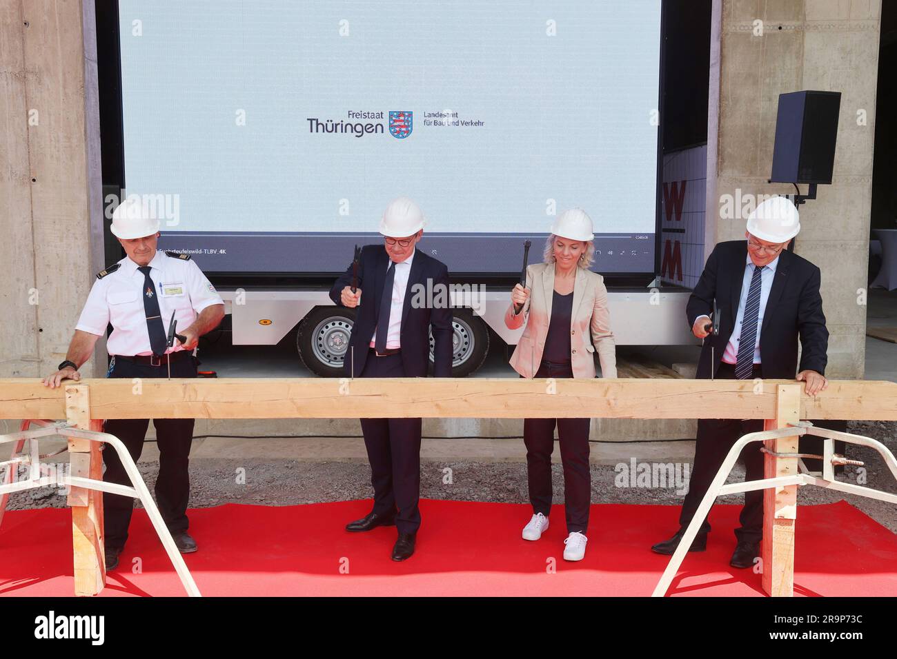 28 June 2023, Thuringia, Bad Köstritz: Jörg Henze, principal, (l-r), Georg Maier (SPD), Minister of the Interior of Thuringia, and Susanna Karawansky, (Die Linke), Minister of Infrastructure in Thuringia, and Hans-Karl Rappel, President of the Thuringian State Office for Construction and Transport, hammer a symbolic nail into a wooden beam at the topping-out ceremony for the construction of a new training and vehicle hall at the Thuringian State Fire and Civil Protection School . The construction project comprises a new two-story building with a training hall and a vehicle hall with ten parkin Stock Photo