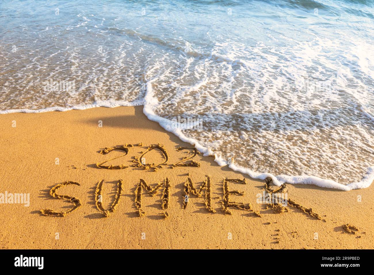Wave washing away the handwritten inscription 2023 Summer on a sandy