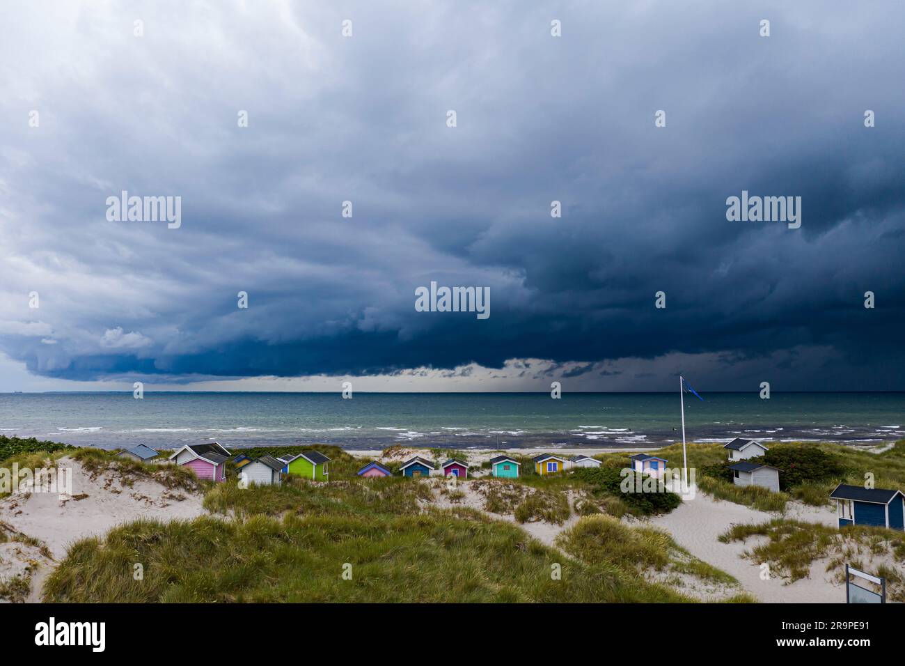 A picturesque shoreline with vibrant beach huts scattered along a sandy pathway extending over the crystal clear waters Stock Photo