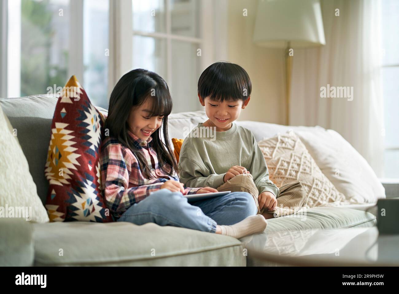 little asian children brother and sister sitting on family couch at home using digital tablet computer together Stock Photo