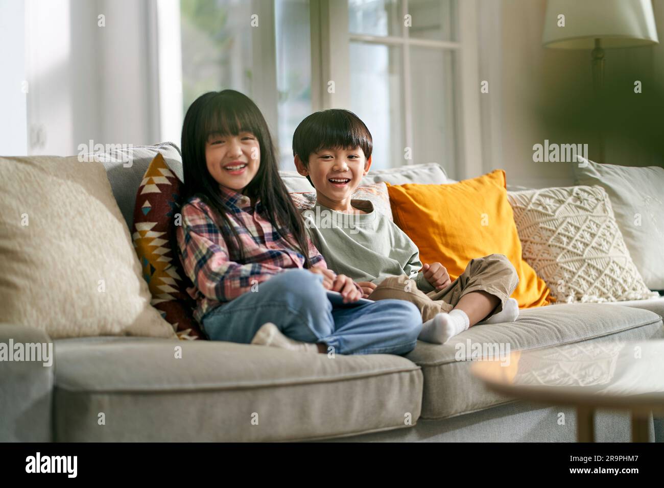 portrait of two asian children brother and sister sitting on family couch at home looking at camera smiling Stock Photo