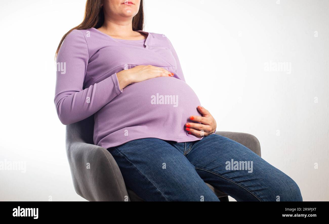 Pregnant girl sits on a chair at the workplace, white background. The