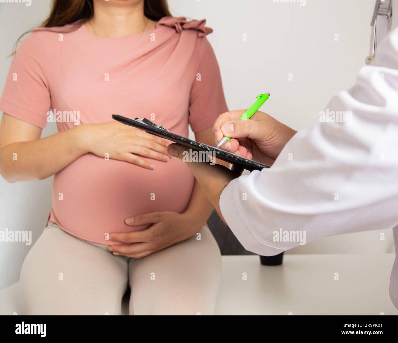 A pregnant girl is being examined by a general practitioner who writes out a list of prescriptions for the nutrition of a pregnant woman. Stock Photo