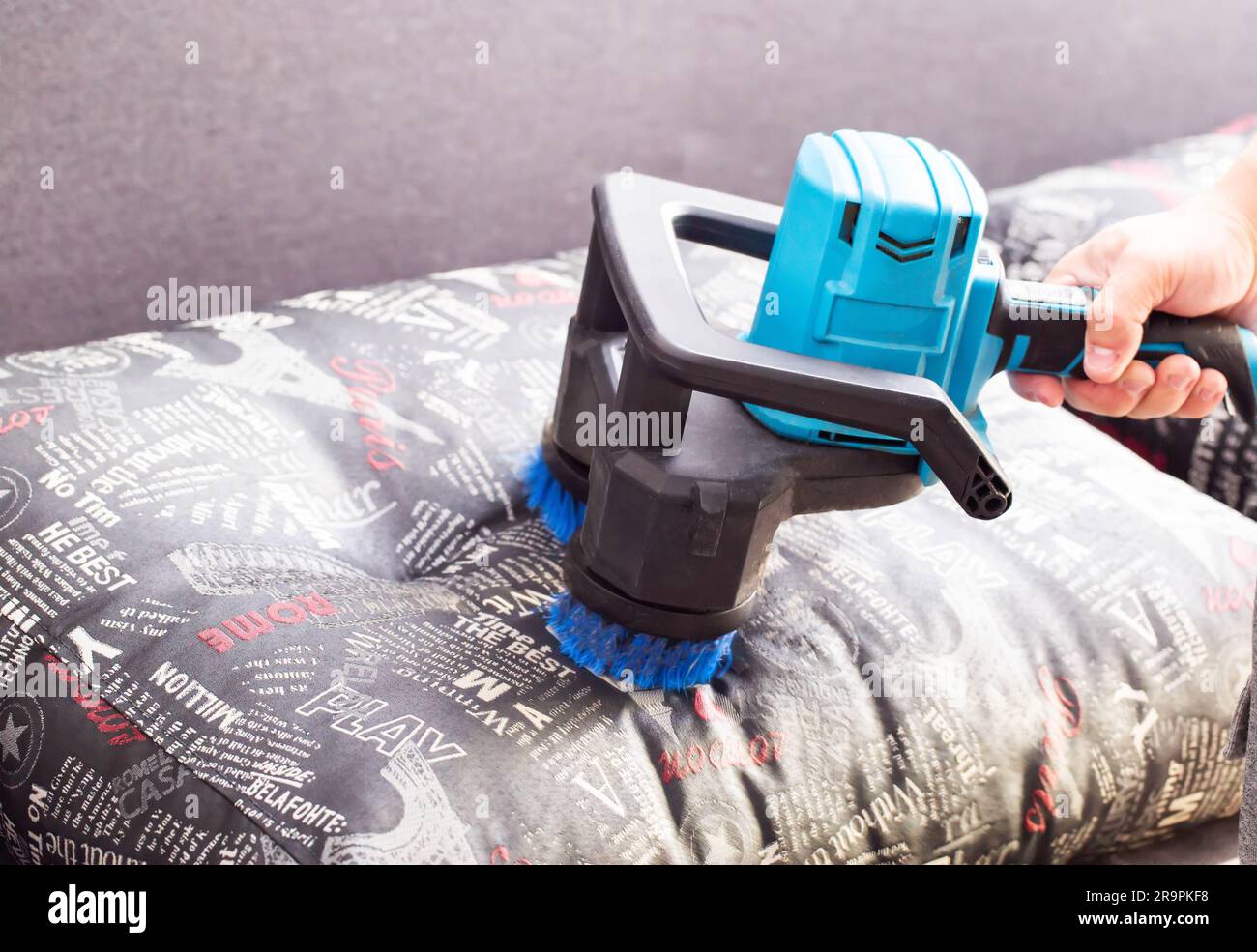 Cleaning sofa cushions with a special electric brush. Dry cleaning of upholstered furniture, close-up. Stock Photo