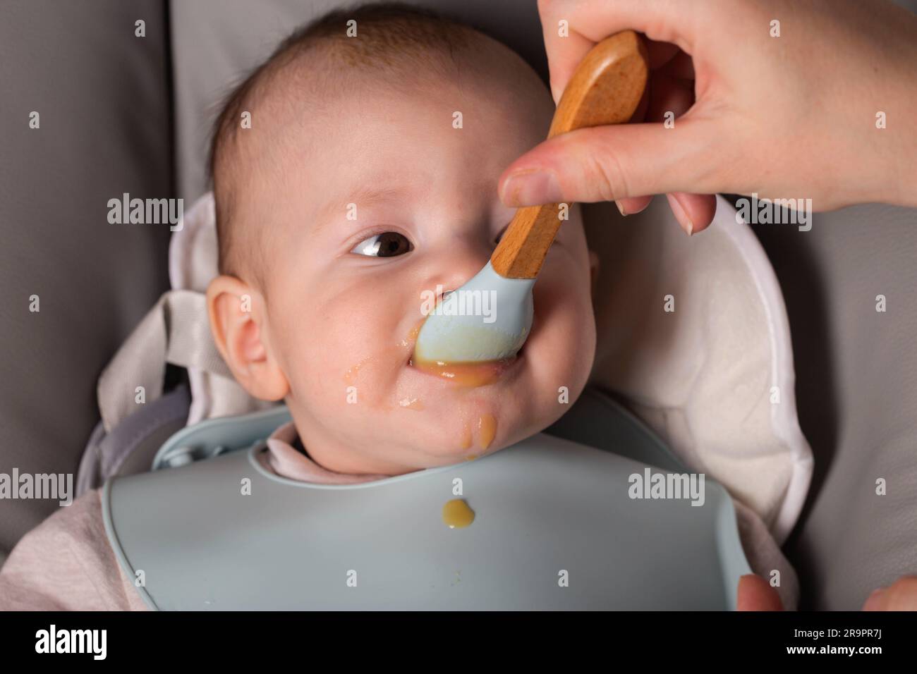 A mother feeds a 6-month-old baby fruit puree. First food for babies