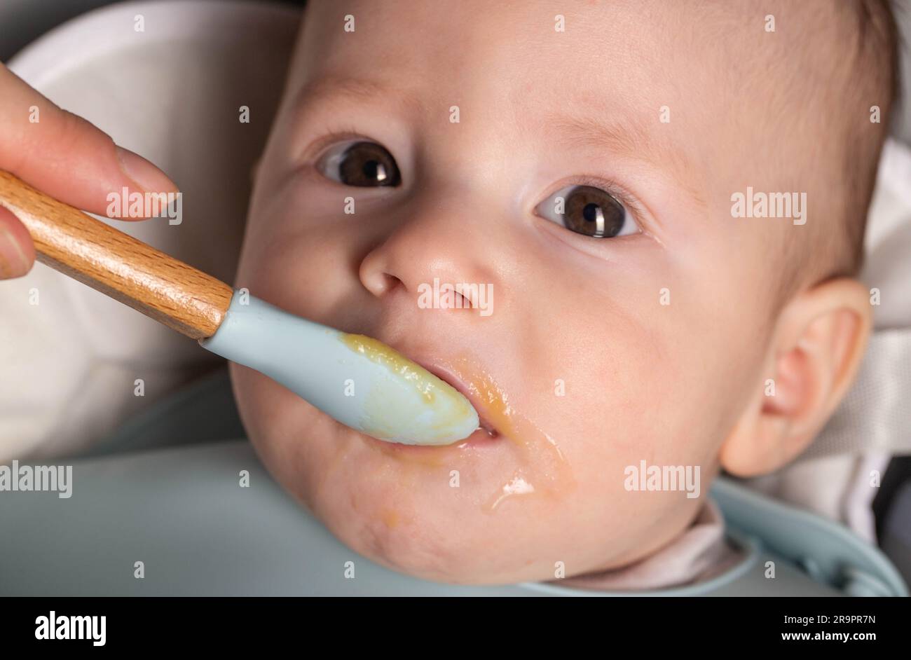 A mother feeds a 6-month-old baby fruit puree. First food for babies