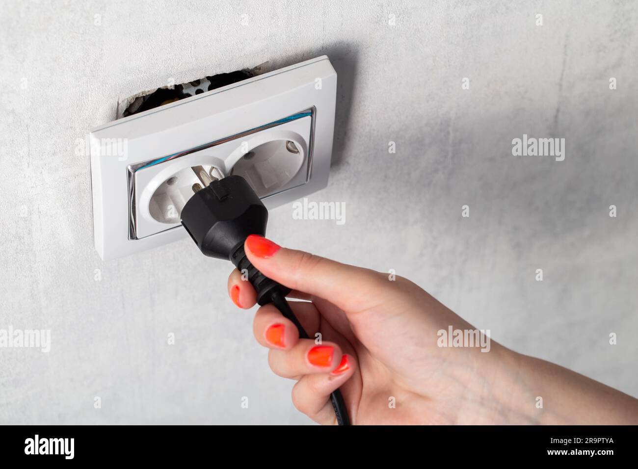 The girl puts the electric plug into a broken socket. Risk of electric ...