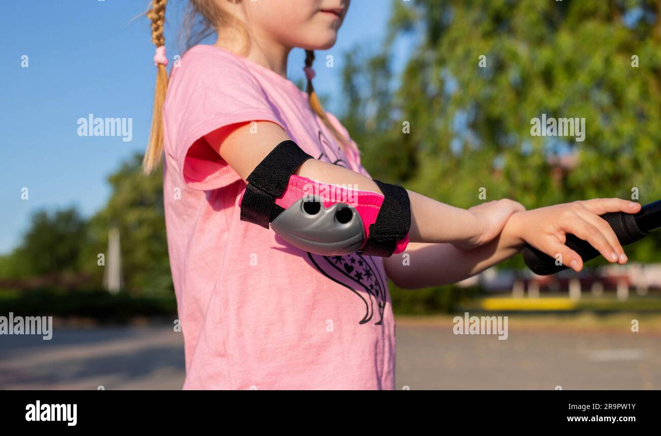pink children's protection on the elbows of a girl who rides a scooter ...