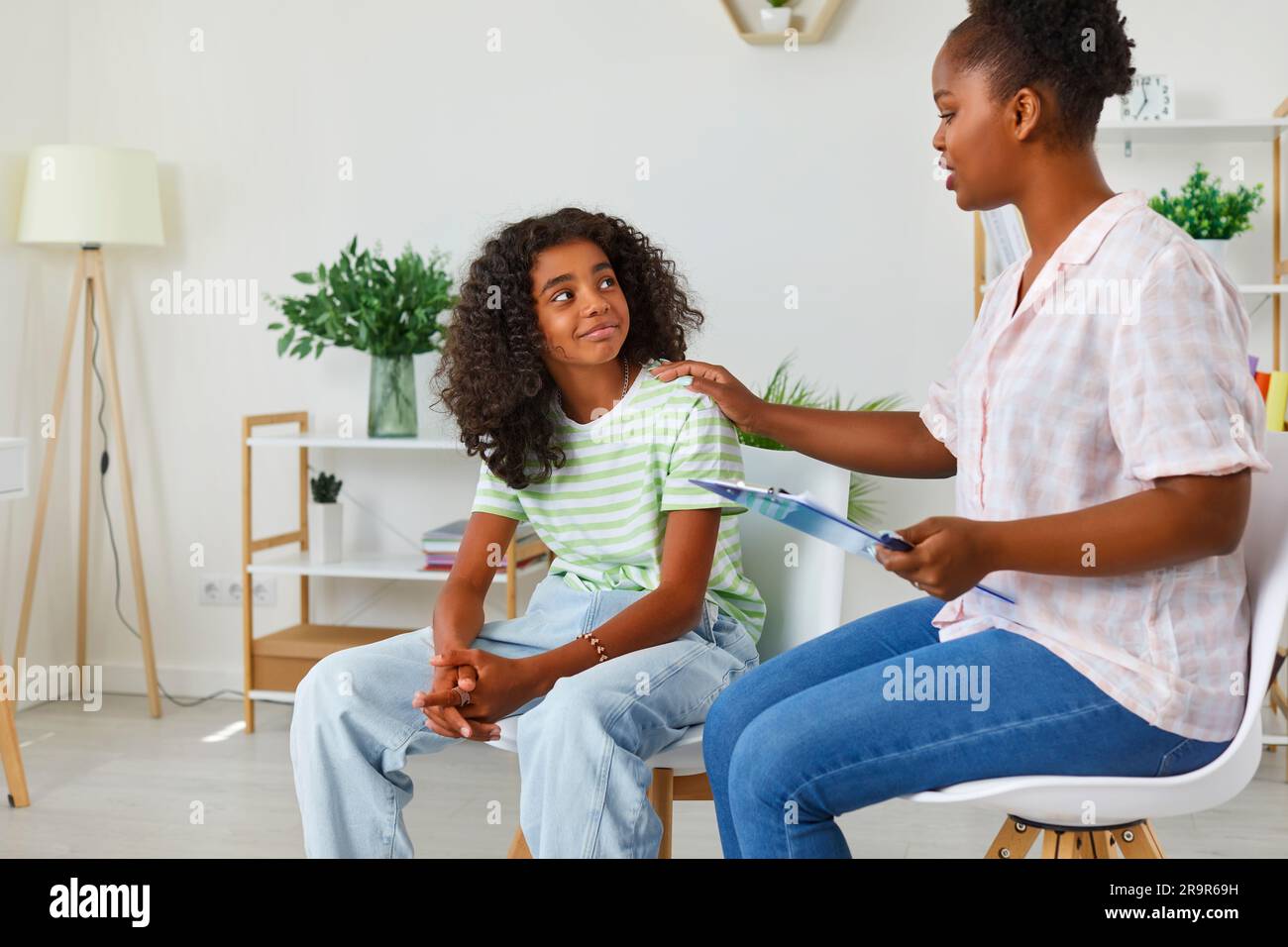 Supporting afro american woman psychologist touching shoulder teen girl on therapy session. Stock Photo