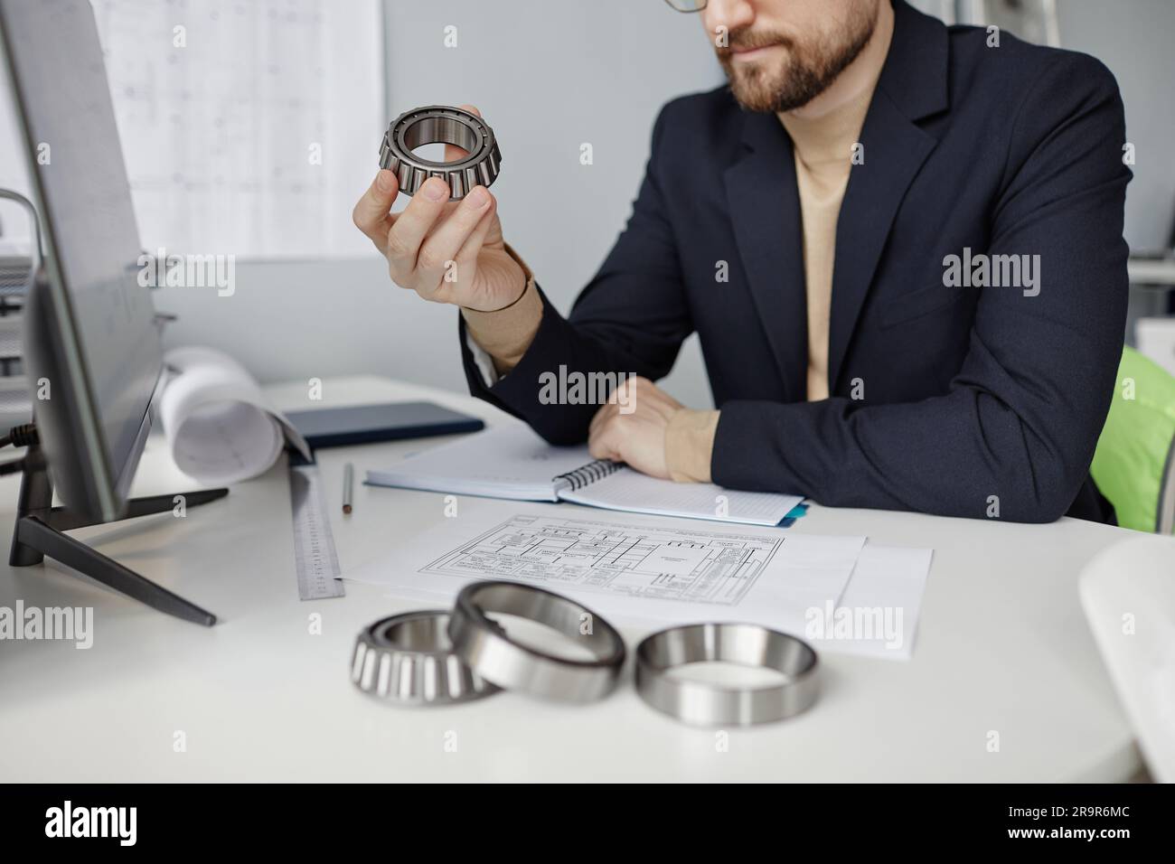 Closeup of mechanical engineer at workplace reviewing blueprints and holding machine part, copy space Stock Photo