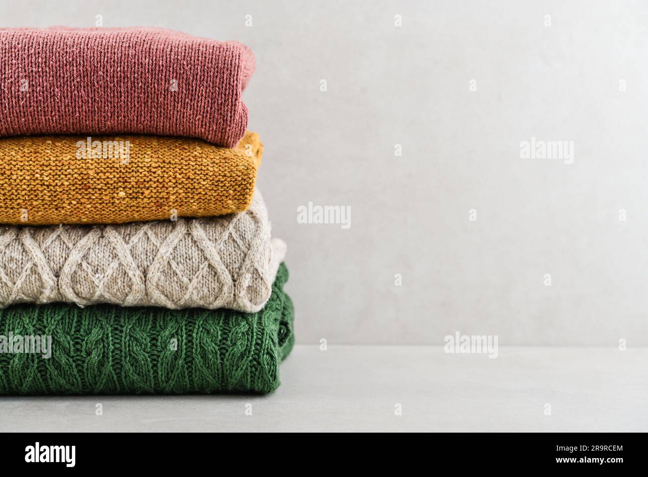 Pile of hand knitted winter clothes on light background: sweaters, knitwear, space for text Stock Photo