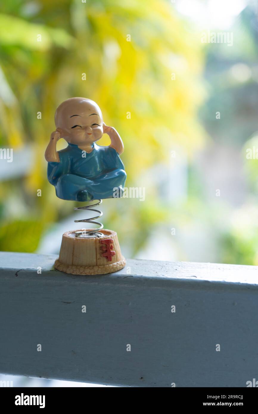 A vertical selective focus shot of a cute praying monk spring figurine on a railing Stock Photo