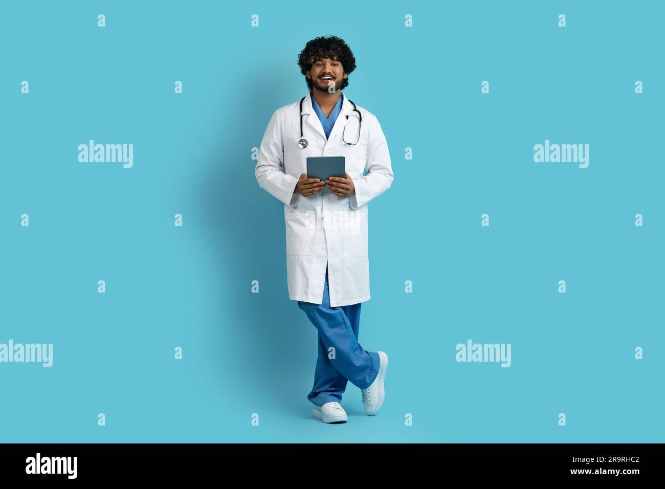 Cheerful indian doctor using digital tablet, blue background Stock Photo