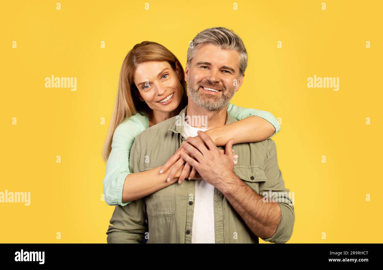 Portrait of happy middle aged woman hugging her husband from behind ...