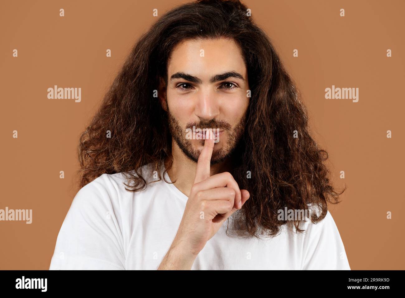 Man With Long Hair Showing Hush Sign Over Brown Background Stock Photo