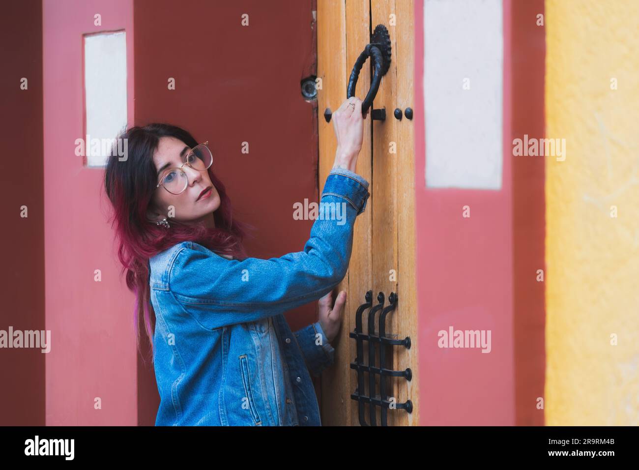 A young female is standing in an indoor doorway of a bright pink house ...