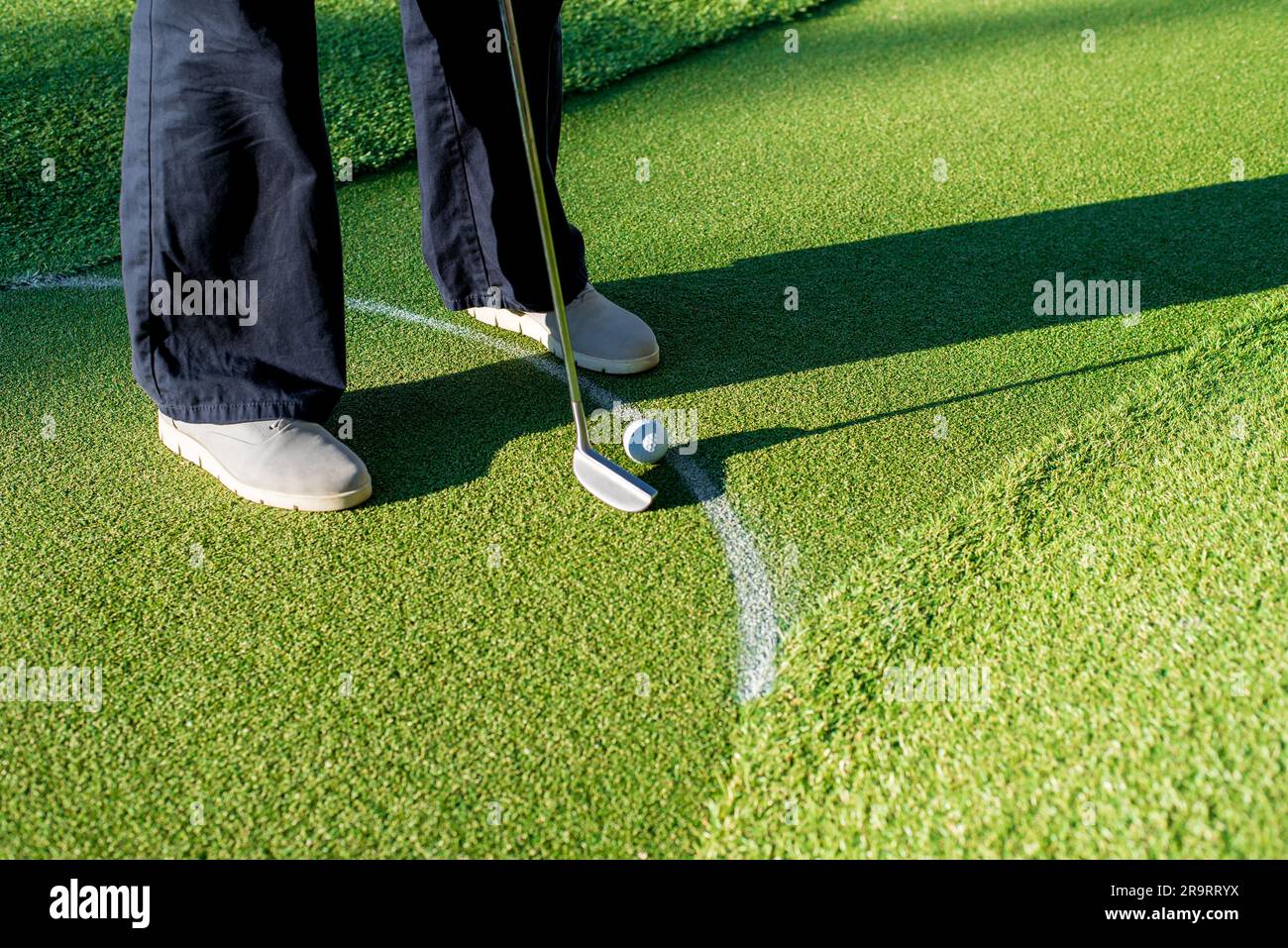 Mini Golf player with grey sneakers putting golf ball into the hole on green lane. Stock Photo