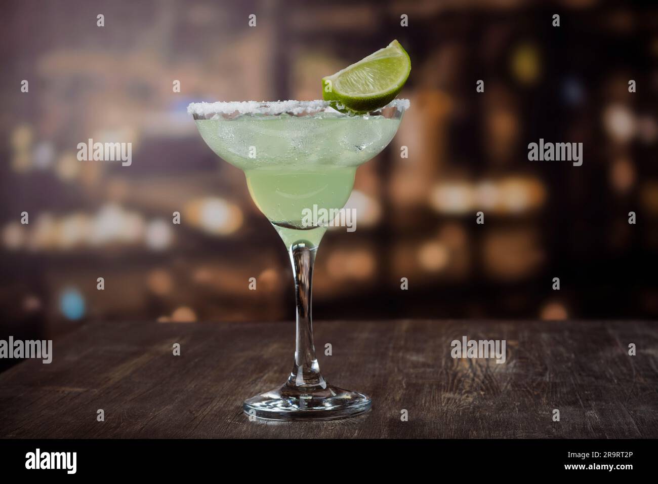 Margarita cocktail with sliced and whole limes on wooden bar table