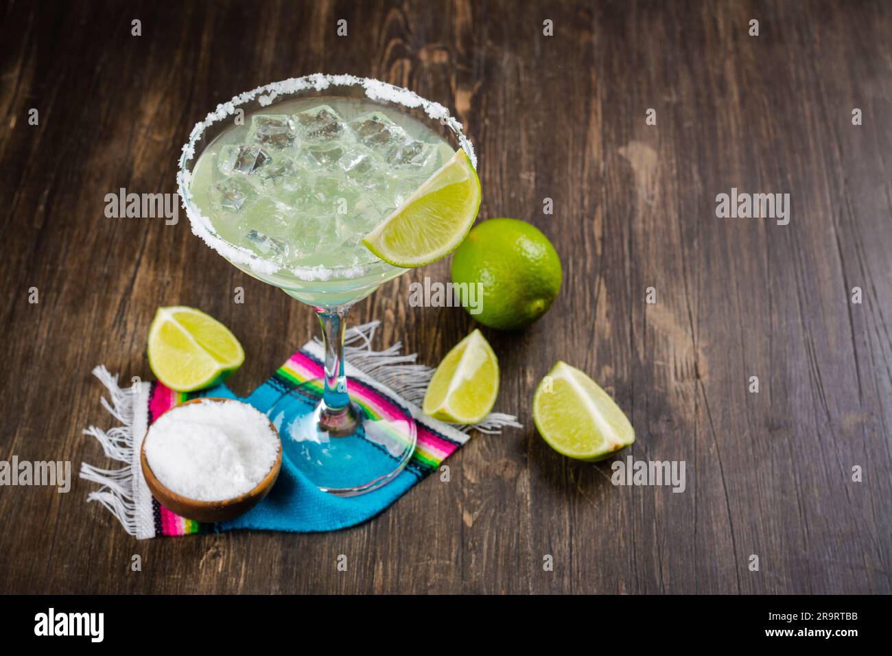 Margarita cocktail with sliced and whole limes on wooden bar table