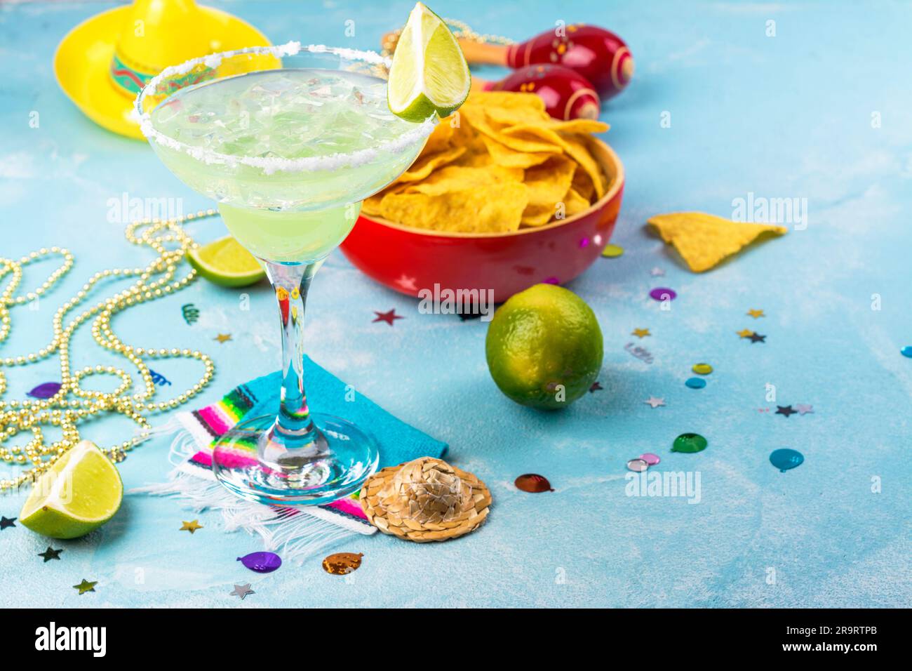 Margarita cocktail with sliced and whole limes, nachos and salt on blue