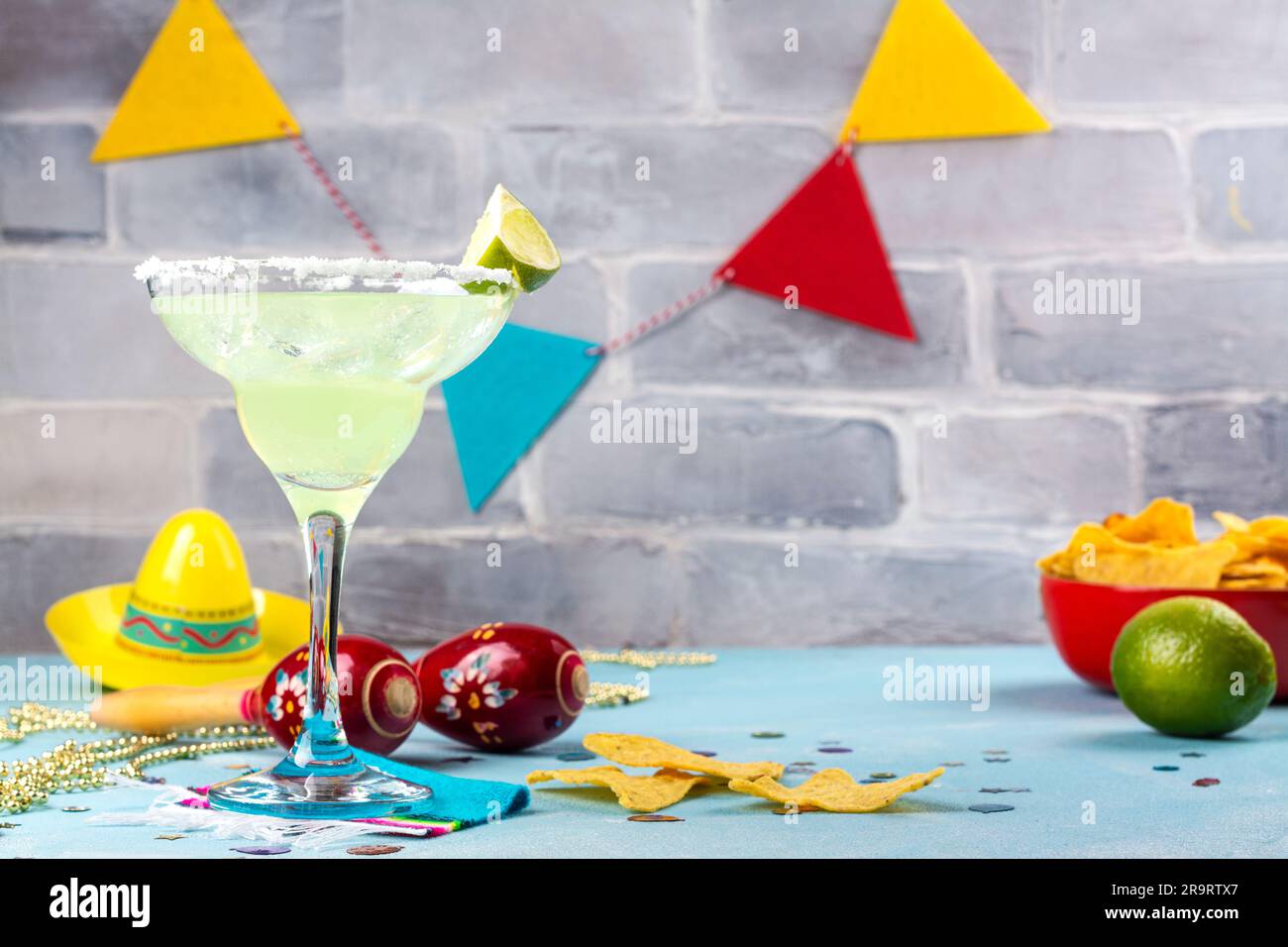 Margarita cocktail with sliced and whole limes, nachos and salt on blue