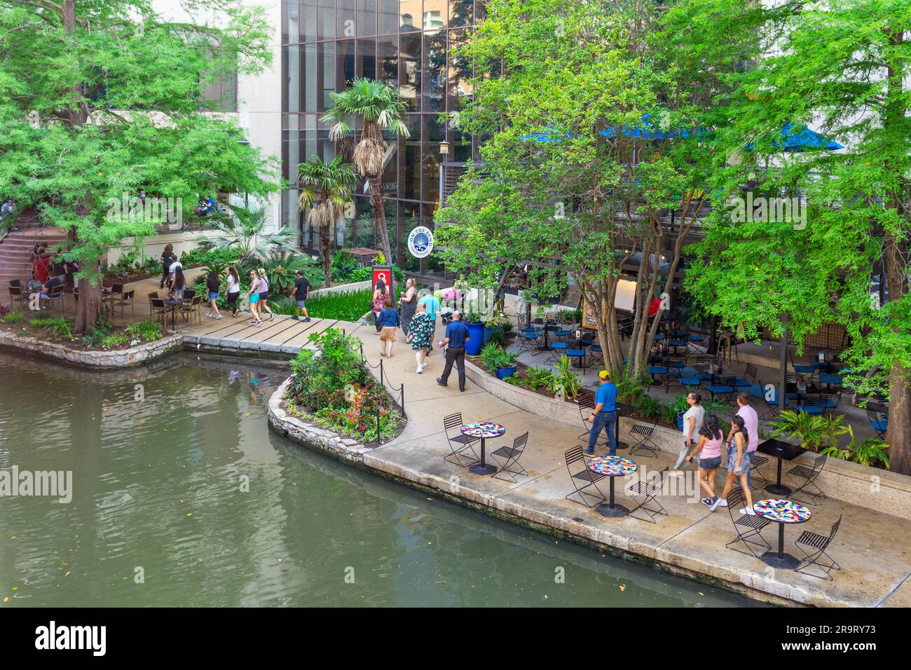 San Antonio, Texas, USA – May 8, 2023: People walking along the San Antonio River Walk in front of the On The Bend Oyster Bar of the Hyatt Regency Hot Stock Photo